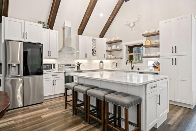 kitchen featuring a kitchen island, white cabinetry, appliances with stainless steel finishes, and wall chimney range hood