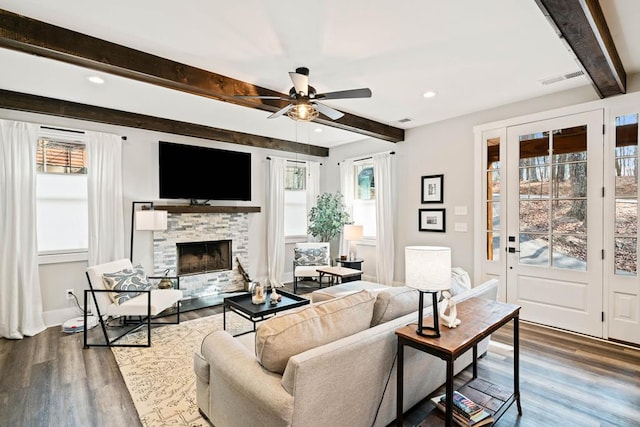 living room featuring ceiling fan, a stone fireplace, dark hardwood / wood-style floors, and beamed ceiling