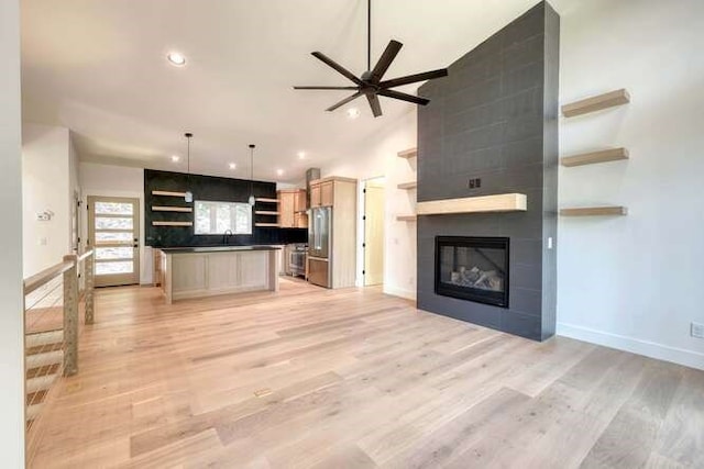 unfurnished living room featuring lofted ceiling, sink, ceiling fan, a tiled fireplace, and light hardwood / wood-style floors