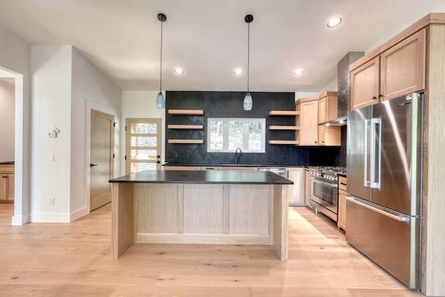 kitchen with light brown cabinetry, decorative light fixtures, a center island, stainless steel appliances, and wall chimney range hood