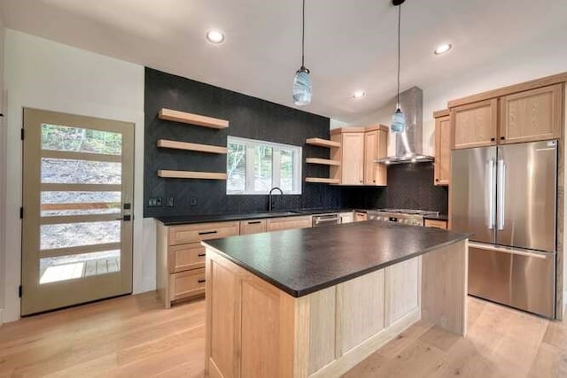 kitchen with stainless steel fridge, hanging light fixtures, a kitchen island, light brown cabinetry, and wall chimney exhaust hood