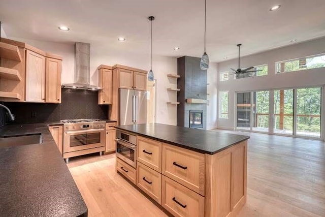 kitchen featuring pendant lighting, light brown cabinetry, decorative backsplash, stainless steel appliances, and wall chimney range hood