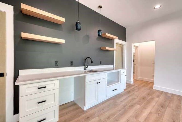 kitchen with pendant lighting, white cabinetry, sink, and light wood-type flooring