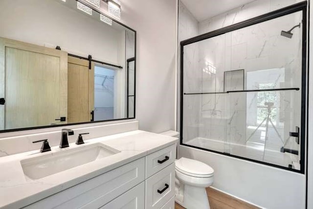 full bathroom featuring hardwood / wood-style flooring, enclosed tub / shower combo, vanity, and toilet