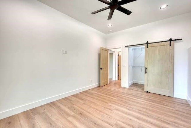 unfurnished bedroom with a closet, light hardwood / wood-style floors, a barn door, and ceiling fan