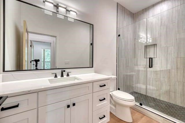 bathroom with a baseboard radiator, vanity, wood-type flooring, a shower with shower door, and toilet