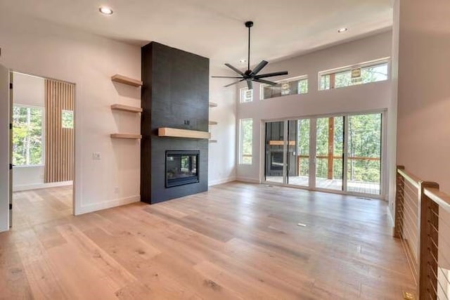 unfurnished living room featuring ceiling fan, a large fireplace, and light hardwood / wood-style floors