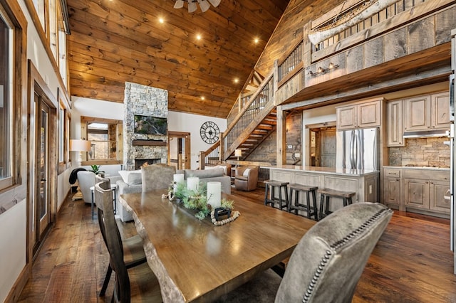 dining room with a stone fireplace, high vaulted ceiling, and dark hardwood / wood-style floors