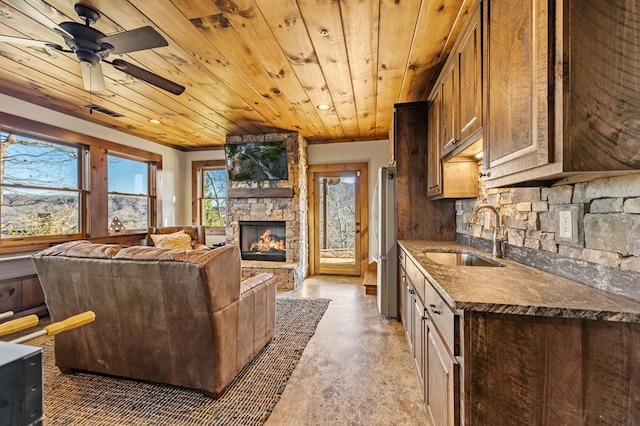 kitchen featuring sink, wood ceiling, stainless steel refrigerator, ceiling fan, and a stone fireplace