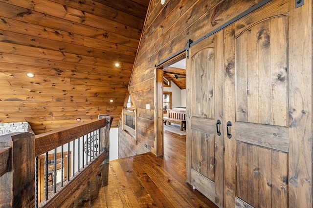 hall with wood ceiling, vaulted ceiling, wood walls, a barn door, and dark hardwood / wood-style floors