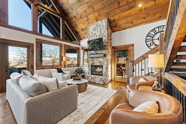 living room with plenty of natural light, high vaulted ceiling, wooden ceiling, and a stone fireplace