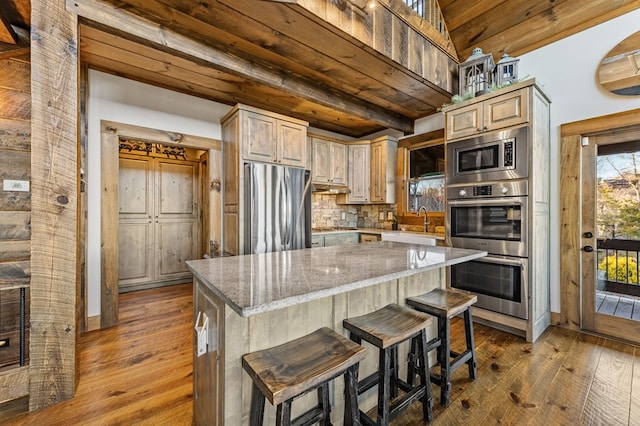 kitchen featuring stainless steel appliances, light brown cabinetry, light stone counters, a kitchen island, and backsplash