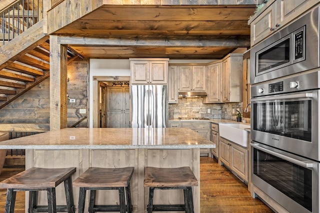 kitchen with stainless steel appliances, hardwood / wood-style floors, a breakfast bar, and light stone counters