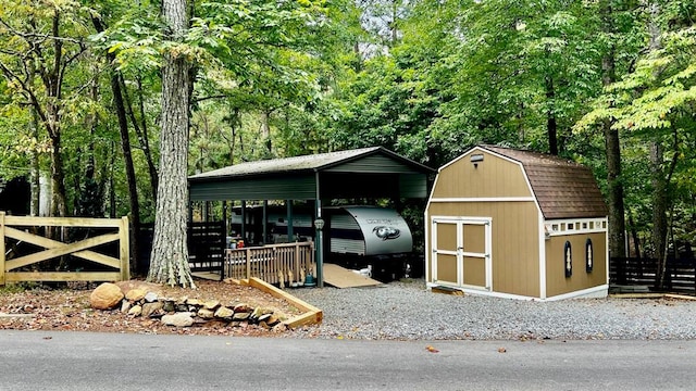 view of shed featuring a detached carport, fence, and a forest view