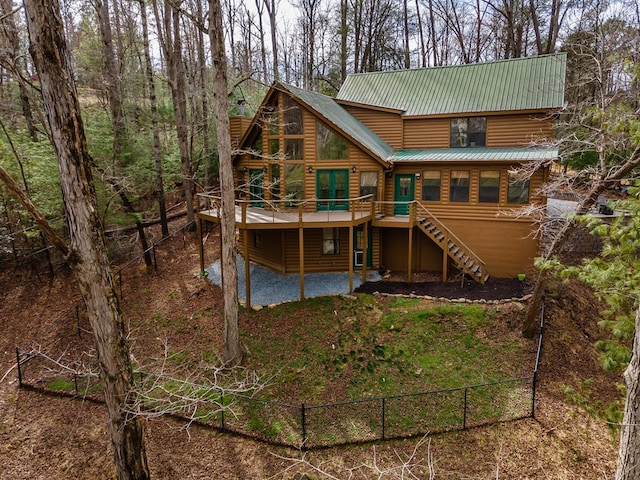 rear view of property featuring faux log siding, fence, a wooden deck, metal roof, and stairs