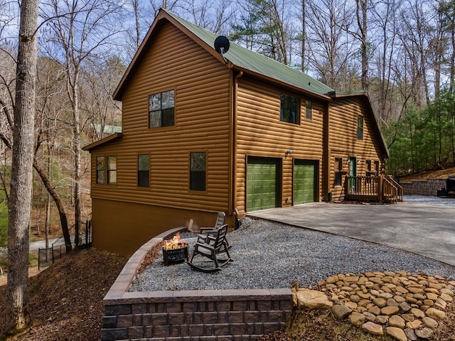 view of property exterior with faux log siding, driveway, an outdoor fire pit, and metal roof