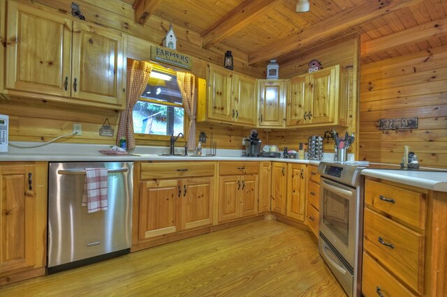 kitchen with wood walls, light countertops, light wood-type flooring, appliances with stainless steel finishes, and a sink