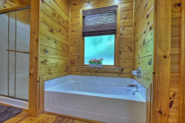 full bathroom with a bath, wood walls, and wood finished floors