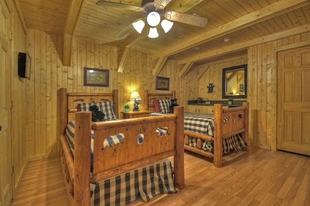 bedroom with beamed ceiling, wooden walls, and wood finished floors