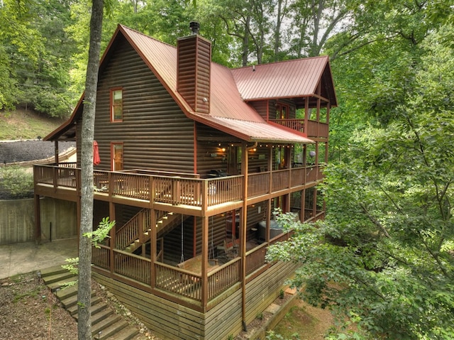 back of property with faux log siding, a chimney, a deck, and metal roof