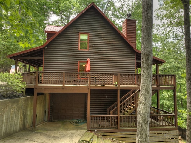 back of property featuring log veneer siding, metal roof, concrete driveway, an attached garage, and a wooden deck