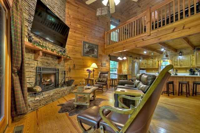 living room featuring visible vents, wood walls, light wood-style flooring, a fireplace, and a ceiling fan