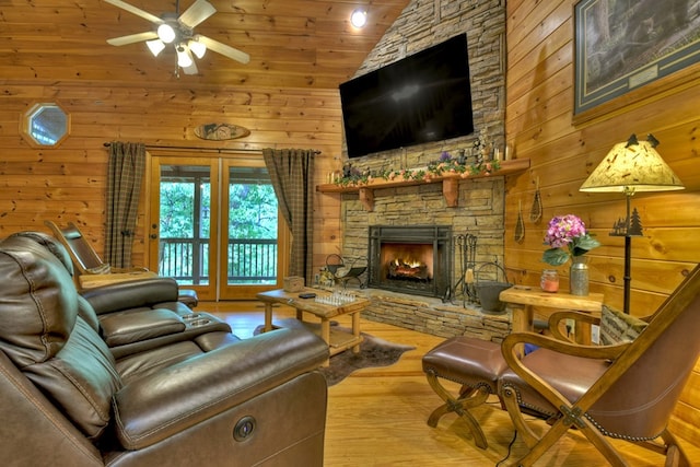 living area with wooden walls, a stone fireplace, wooden ceiling, wood finished floors, and a ceiling fan