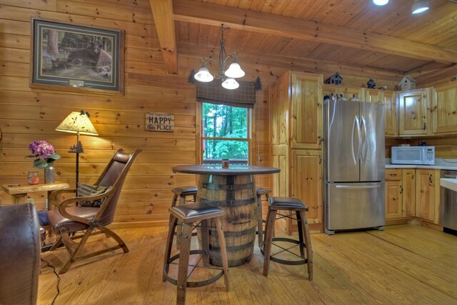 kitchen featuring beamed ceiling, white microwave, light wood-type flooring, and freestanding refrigerator