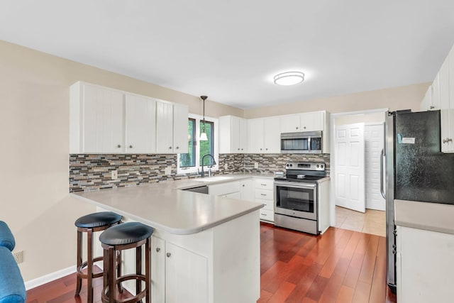 kitchen featuring stainless steel appliances, a peninsula, a sink, dark wood-style floors, and tasteful backsplash