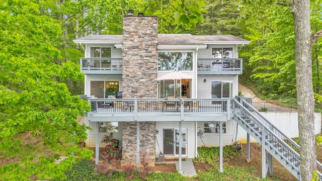 rear view of house with a balcony, stairway, a chimney, and stone siding
