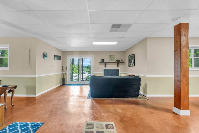 living room featuring concrete floors, a drop ceiling, and baseboards