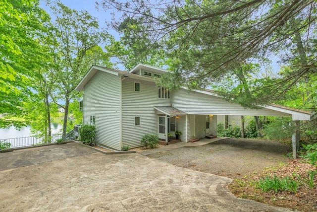 mid-century modern home with concrete driveway, a water view, a carport, and fence