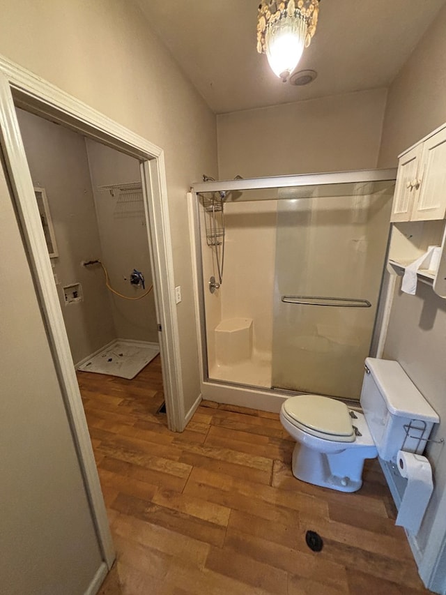 bathroom with a shower stall, toilet, and wood finished floors