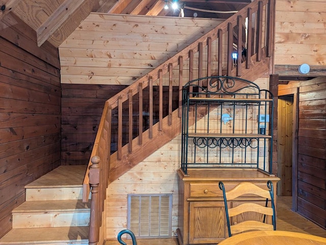 stairway with lofted ceiling with beams, wood ceiling, and wooden walls