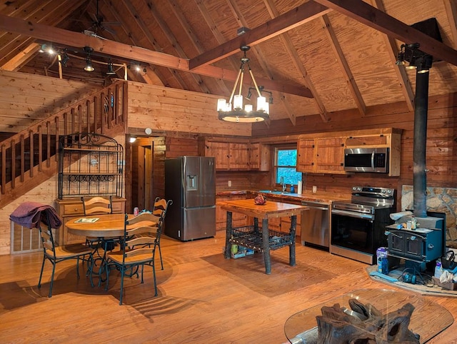 kitchen featuring appliances with stainless steel finishes, wooden walls, high vaulted ceiling, light hardwood / wood-style floors, and a wood stove