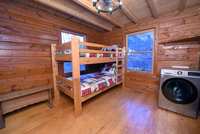 bedroom with beam ceiling, wood walls, wood ceiling, light hardwood / wood-style flooring, and washer / clothes dryer