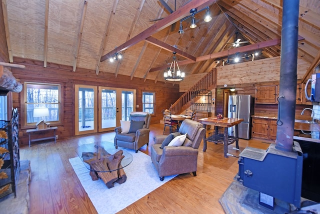 living room featuring wood walls, wood ceiling, a wood stove, beam ceiling, and light hardwood / wood-style floors