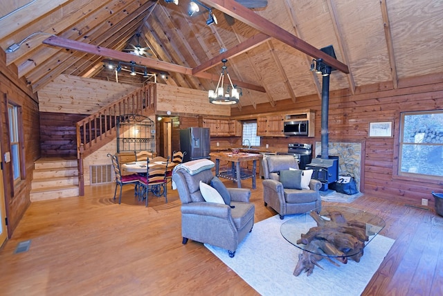 living room featuring wood ceiling, wood walls, light hardwood / wood-style floors, beamed ceiling, and a wood stove