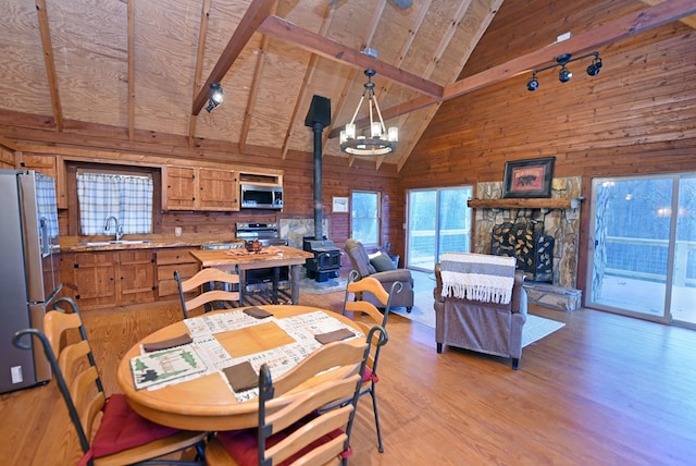 dining room featuring sink, wood ceiling, a wood stove, wooden walls, and beamed ceiling