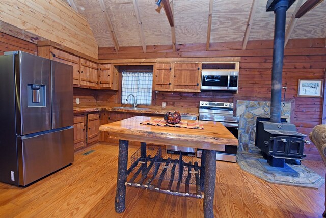 kitchen featuring wood walls, a wood stove, vaulted ceiling with beams, stainless steel appliances, and light hardwood / wood-style flooring