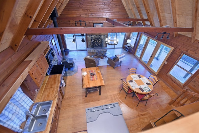 living room featuring high vaulted ceiling, wood walls, a wood stove, a notable chandelier, and beam ceiling