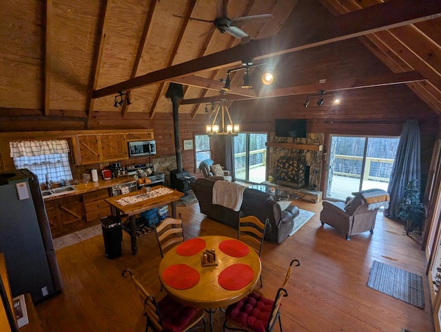 dining room featuring a wood stove, ceiling fan, vaulted ceiling with beams, wood-type flooring, and wood walls