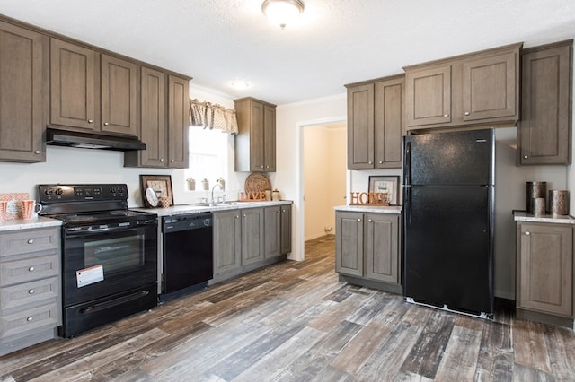 kitchen featuring dark wood-style flooring, a sink, light countertops, under cabinet range hood, and black appliances