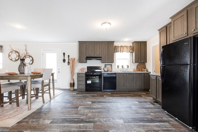kitchen featuring a sink, light countertops, dark wood finished floors, under cabinet range hood, and black appliances