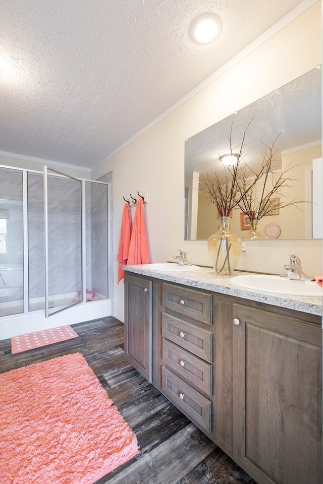 bathroom with crown molding, a sink, a textured ceiling, wood finished floors, and a stall shower