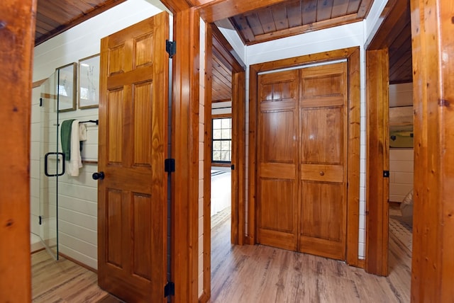 corridor with light hardwood / wood-style floors, wooden walls, and wood ceiling