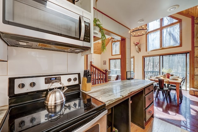 kitchen with light wood-style flooring, appliances with stainless steel finishes, light stone counters, a high ceiling, and a notable chandelier