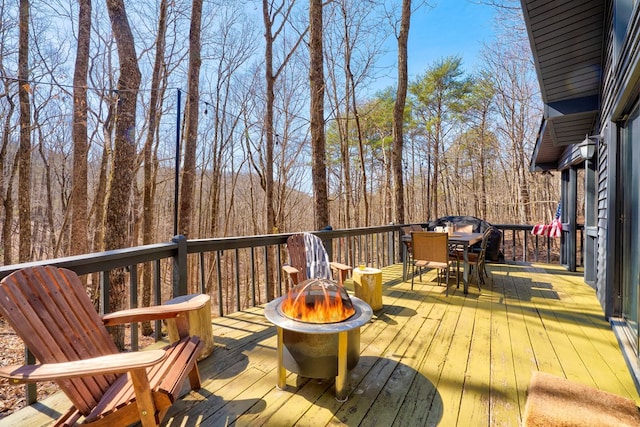 wooden terrace featuring an outdoor fire pit, outdoor dining area, and a view of trees