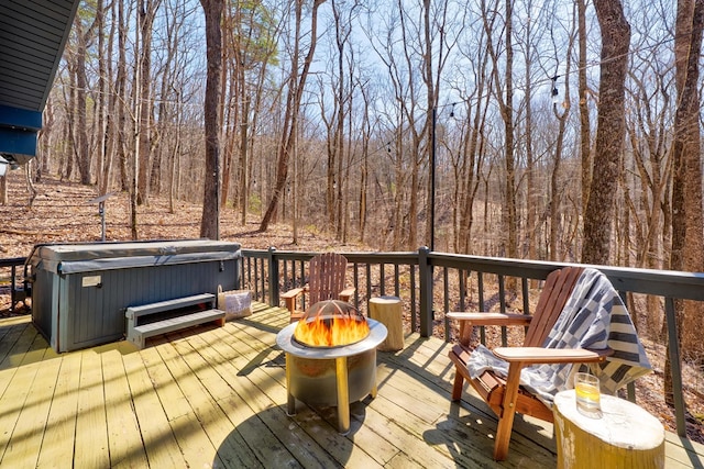 wooden deck with an outdoor fire pit, a hot tub, and a view of trees