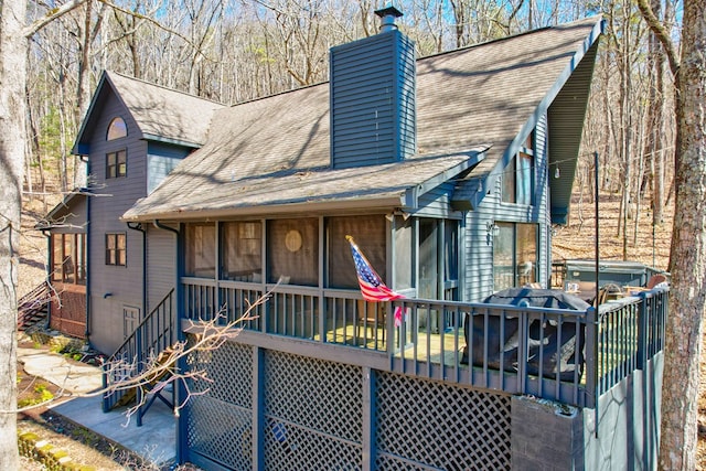 view of front of home featuring a shingled roof, a sunroom, a jacuzzi, a chimney, and a deck